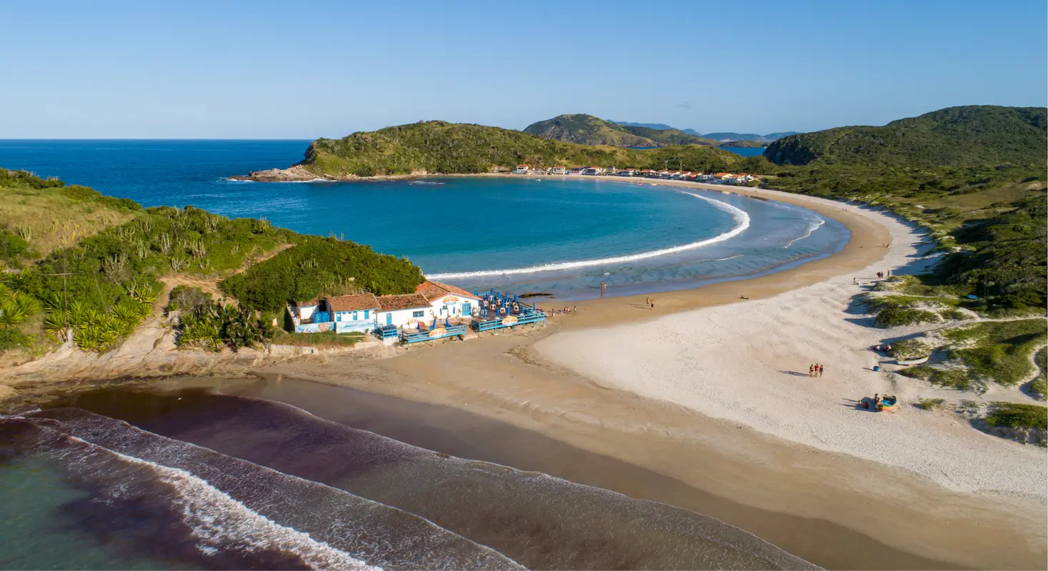 Vista aérea de Cabo Frio com praia de águas cristalinas, areia clara e vegetação costeira preservada.