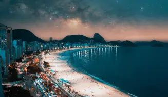 Praia de Copacabana á noite, mostrando os prédios, a faixa de areia e o mar.