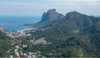Vista aérea de são conrado com montanhas, vegetação preservada, praia, mar azul e prédios residenciais luxuosos.